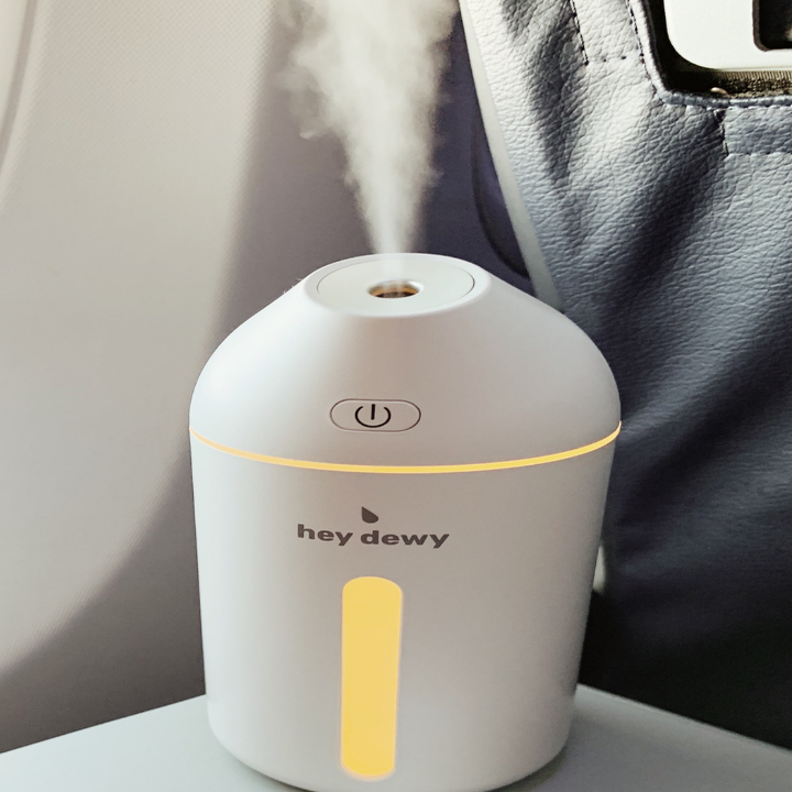 a white Hey Dewy humidifier with water vapor spewing out the top and the front panel illuminated 