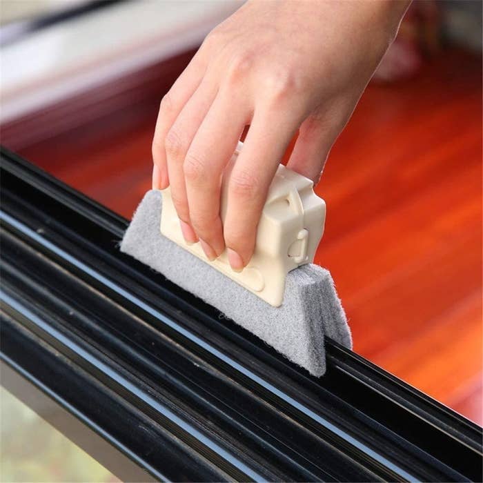 model hand holding a scrubber that fits snugly on top of a windowsill groove