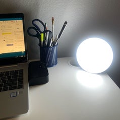 a reviewer photo of a desk with a round illuminated light sitting on the corner 