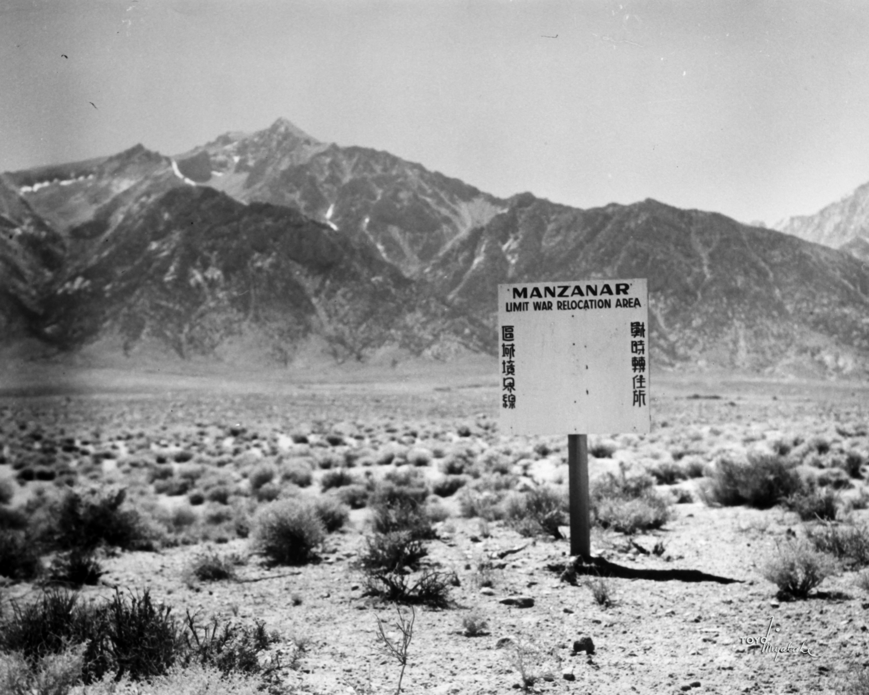 Mountains in distance and a sign in a desert that reads &quot;Manzanar Unit War Relocation Area&quot;