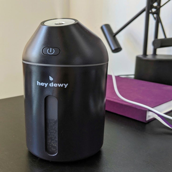 a black Hey Dewy humidifier sitting on a desk in front of a purple notebook 