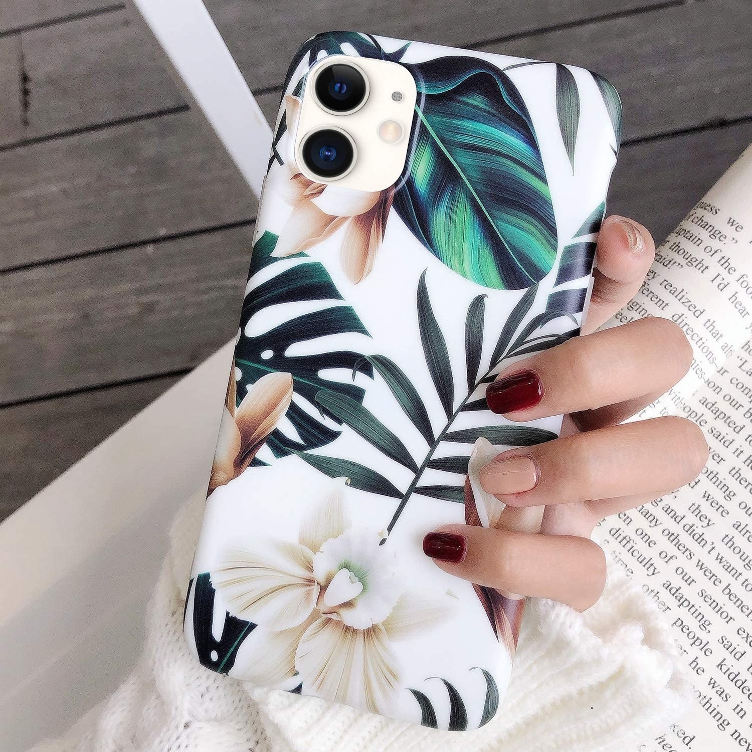 a model holding a white iphone case with green leaves and white flowers on it