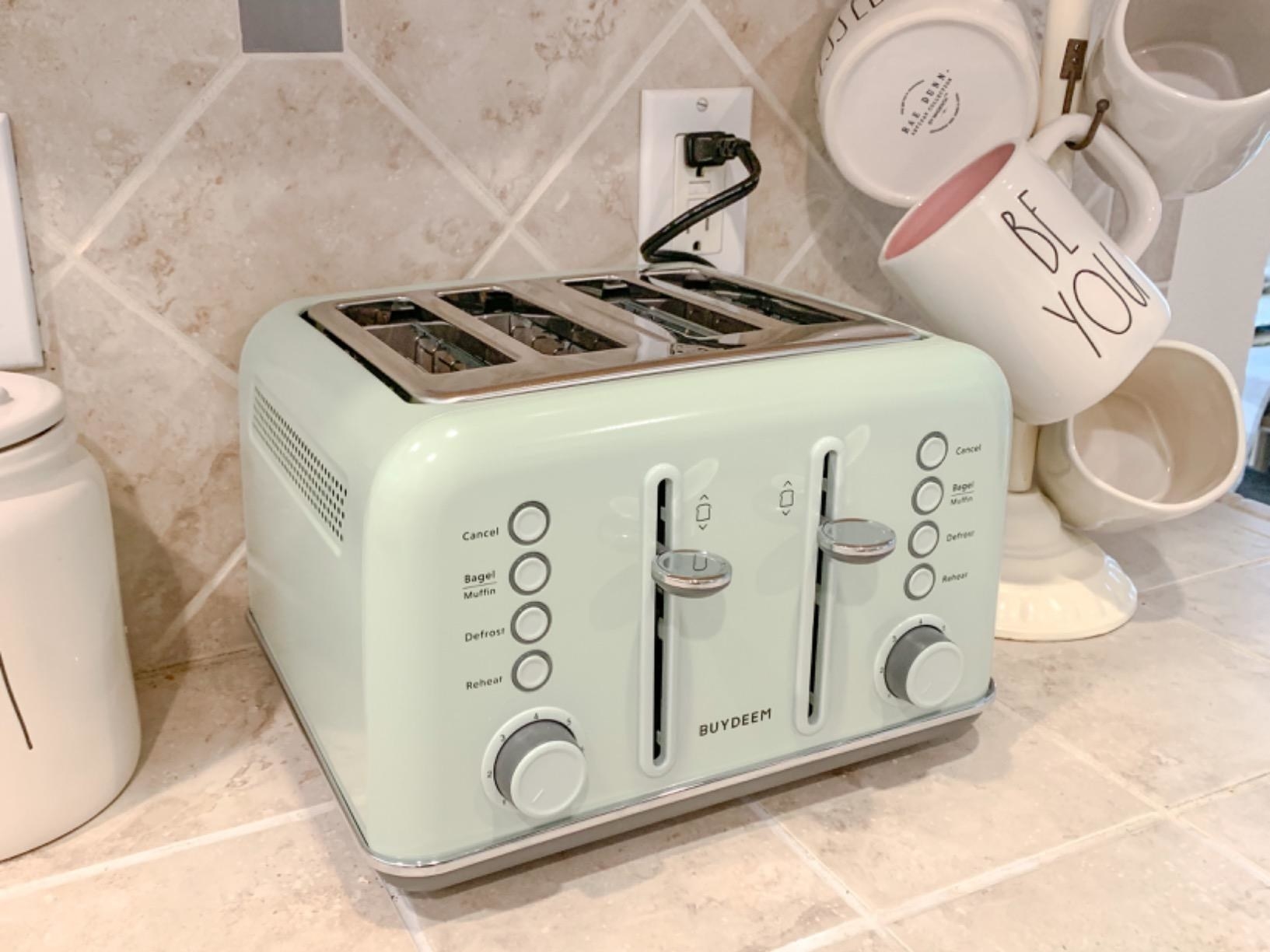 reviewer image of the cozy greenish BuyDeem four slice retro toaster on a kitchen counter