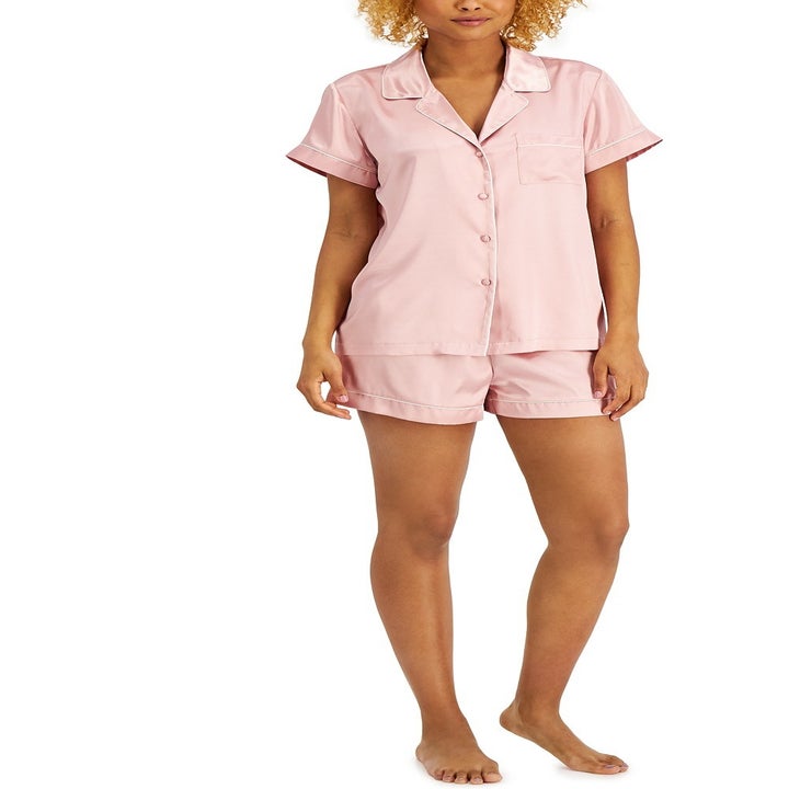 a  model wearing a satin pajama set, including a pink buttoned short-sleeve top and matching shorts