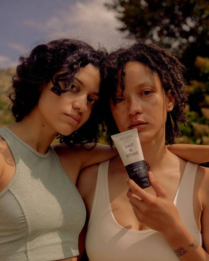A pair of models holding up a tube of the sunscreen while looking into the camera