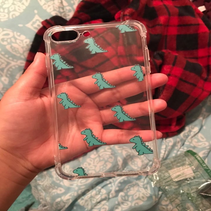 a reviewer holding the clear phone case with tiny green dinosaurs on it