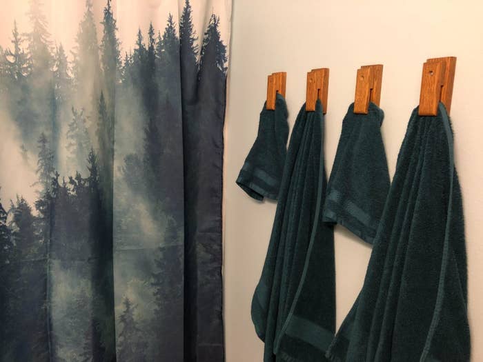 The green towels hung up next to a forest-printed shower curtain