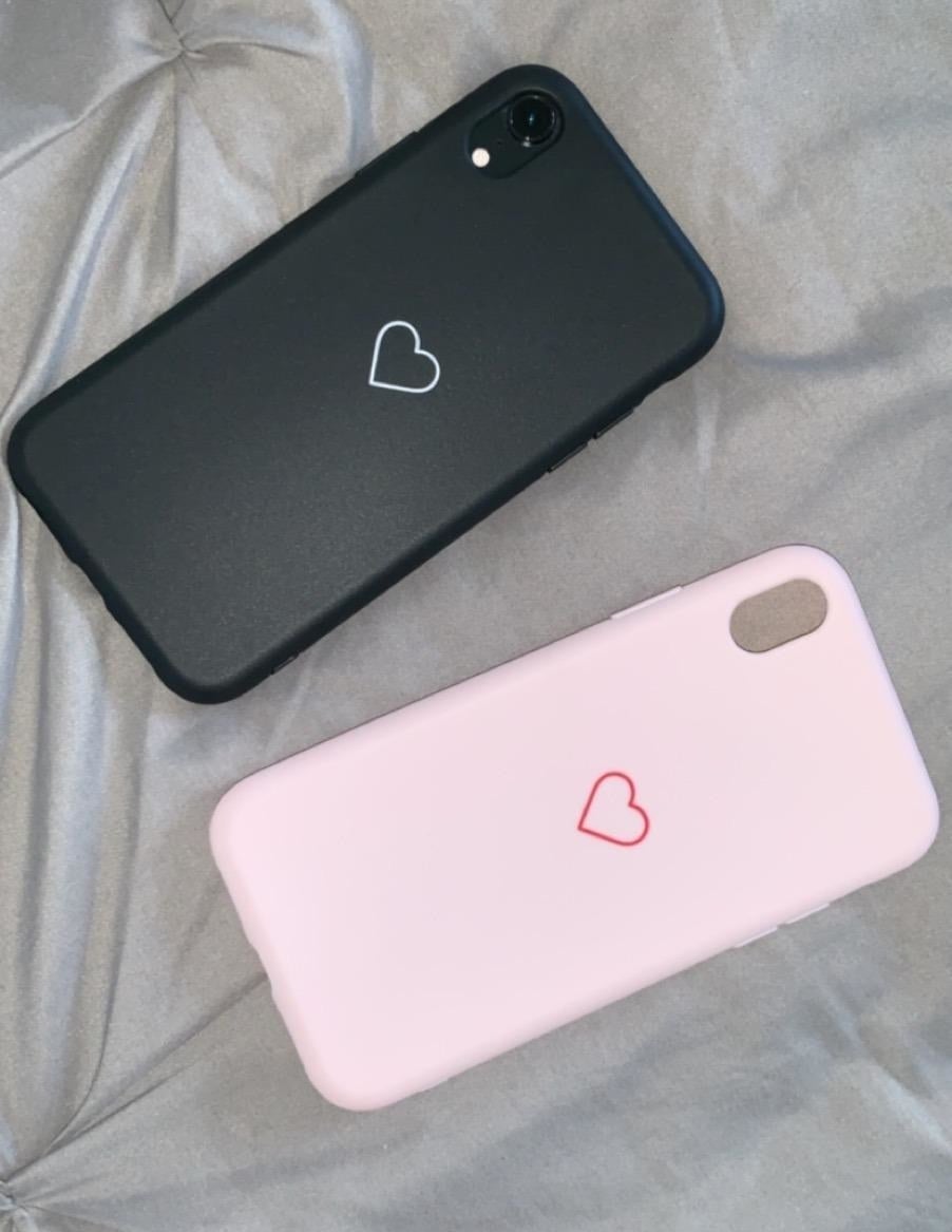 a black phone case with a small white heart on the back and a pink case with a small red heart on the back