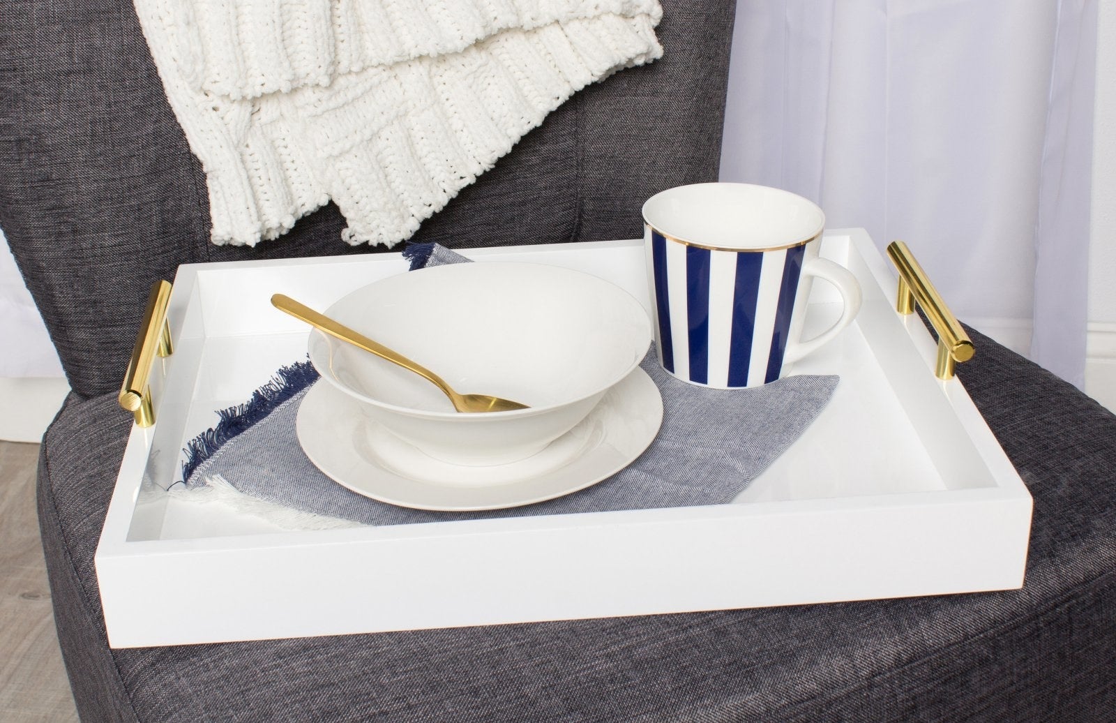 White decorative tray with gold handles on chair with bowl and cup
