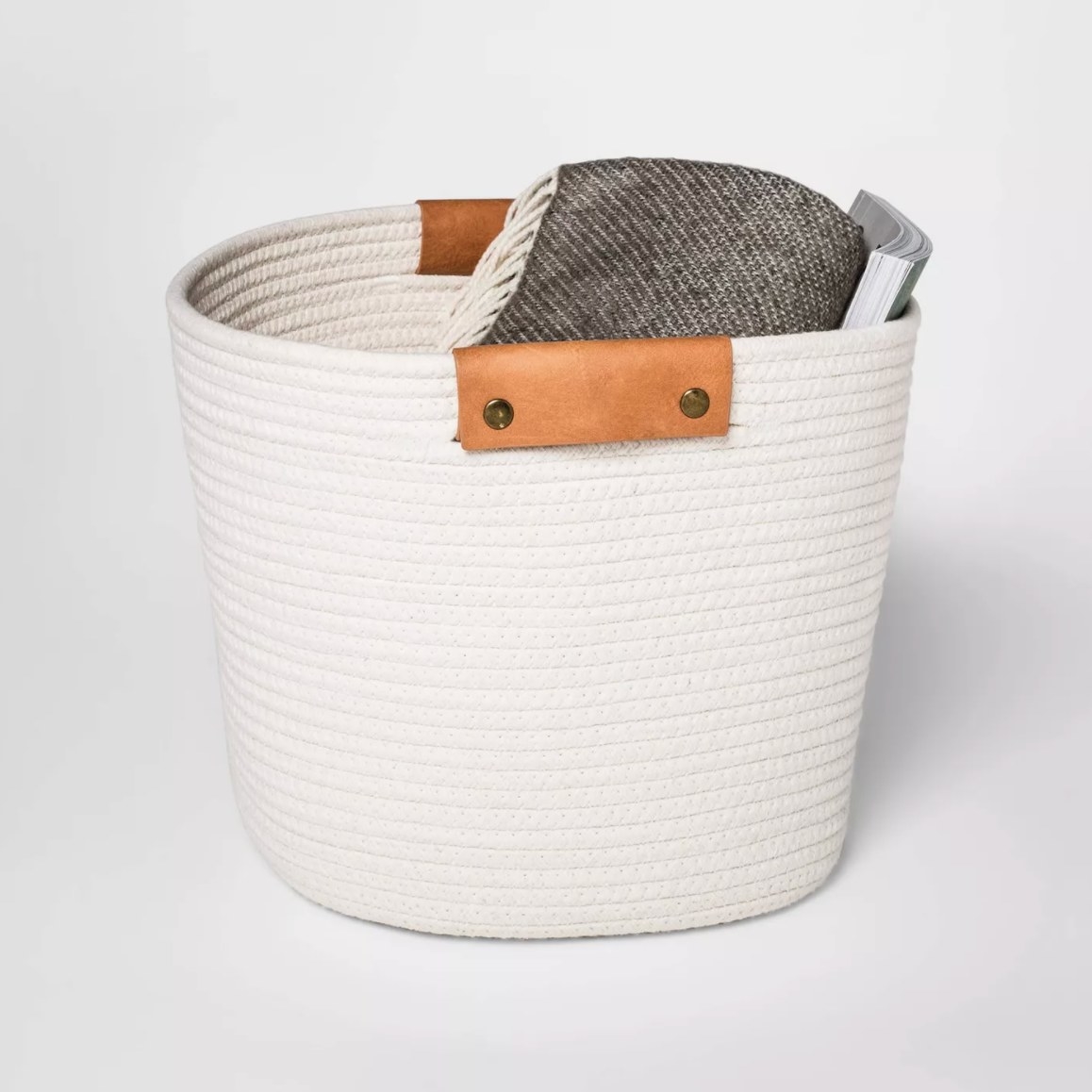 The cream rope basket which has leather handles holding a blanket and magazine