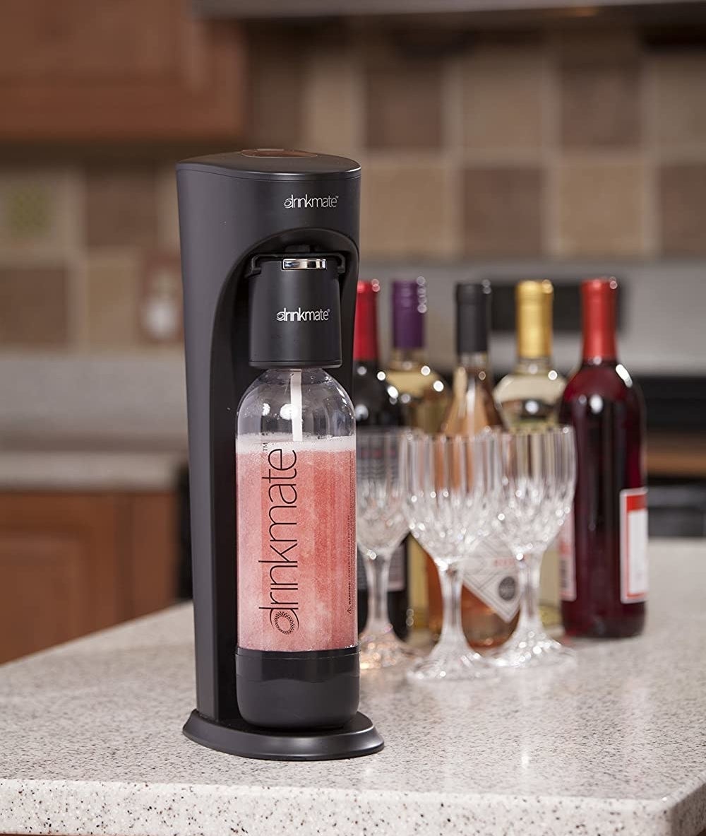 the DrinkMate carbonated beverage maker on a counter in front of several bottles of wine