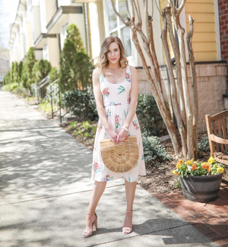 Person is wearing a white floral dress and holding a bamboo handbag