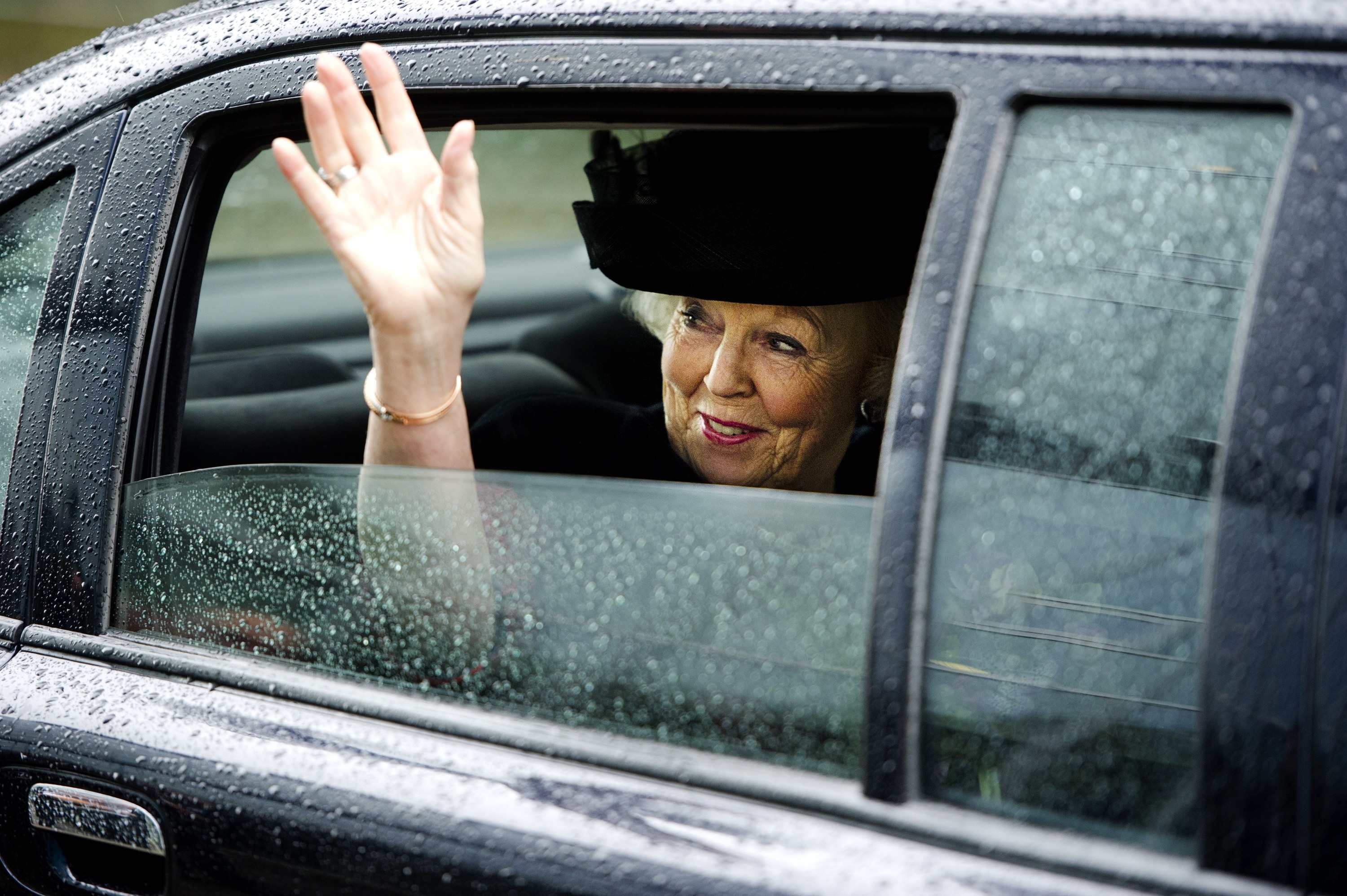 Queen waving out of a sleek black car