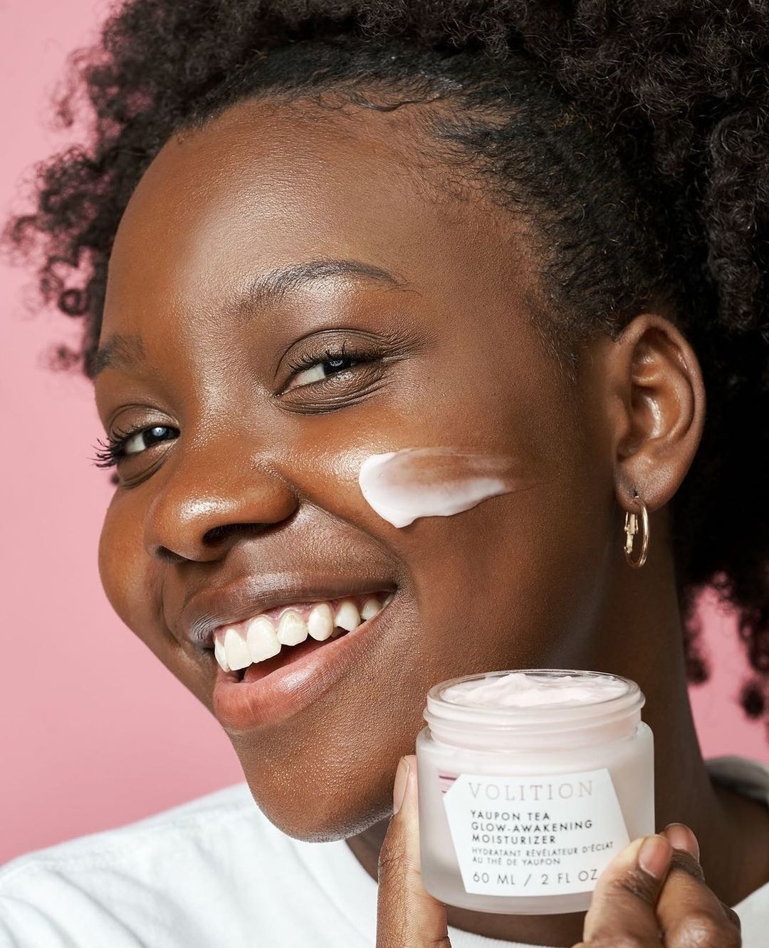 A smiling person applying the cream to their face
