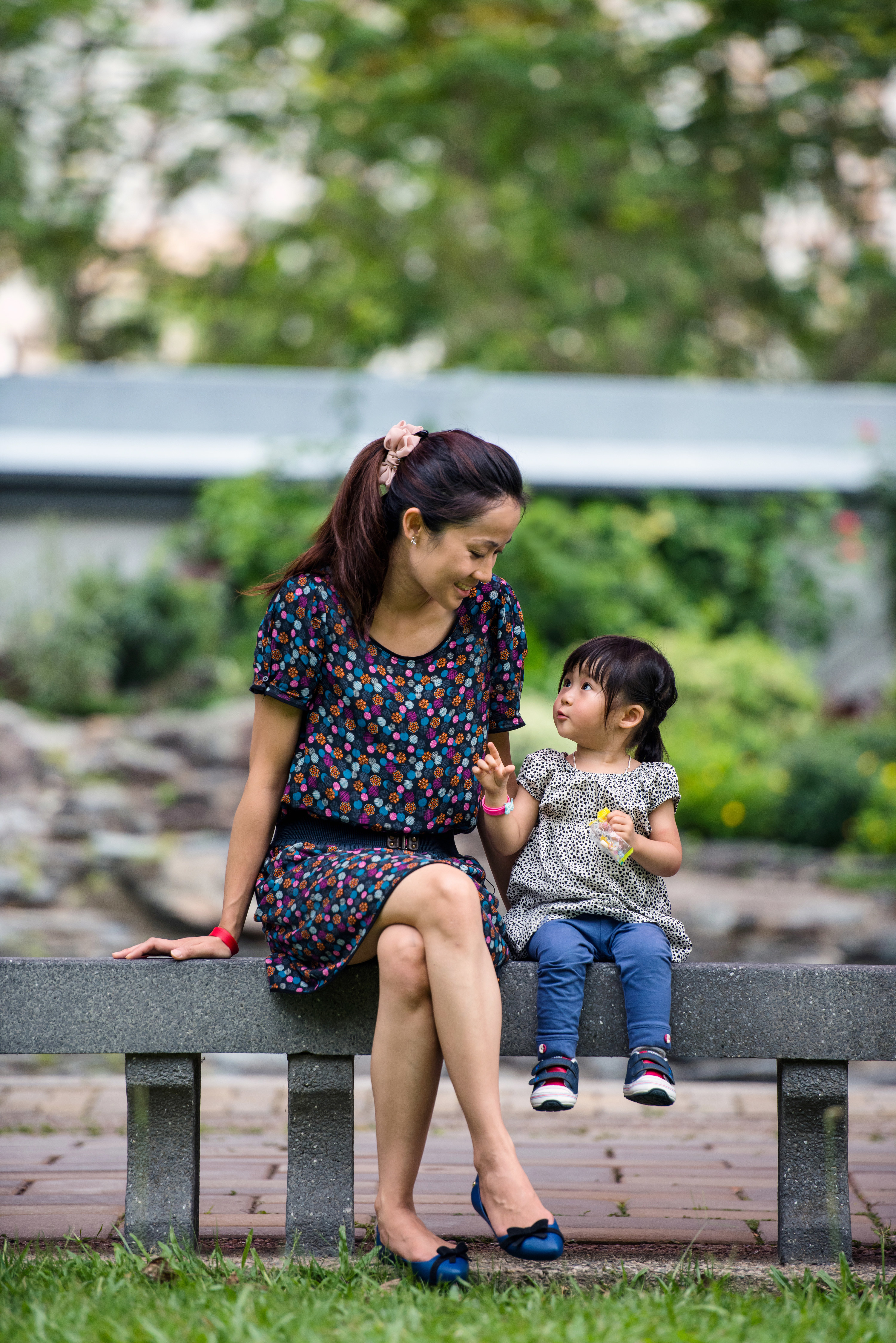 Asian mother talking to her toddler, while sitting on a stone bench in the park