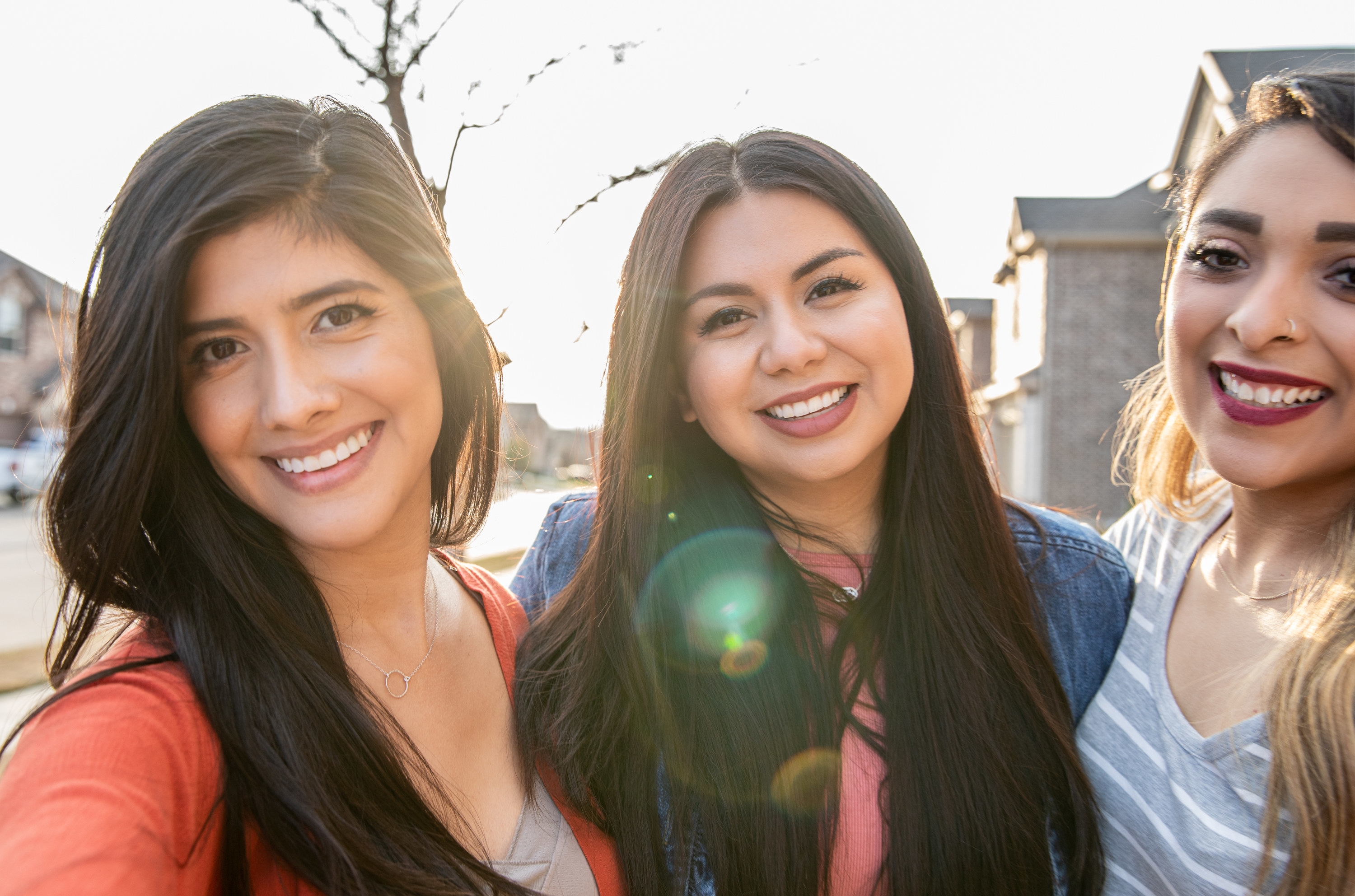 Three Latinx women smiling at the camera outside their home