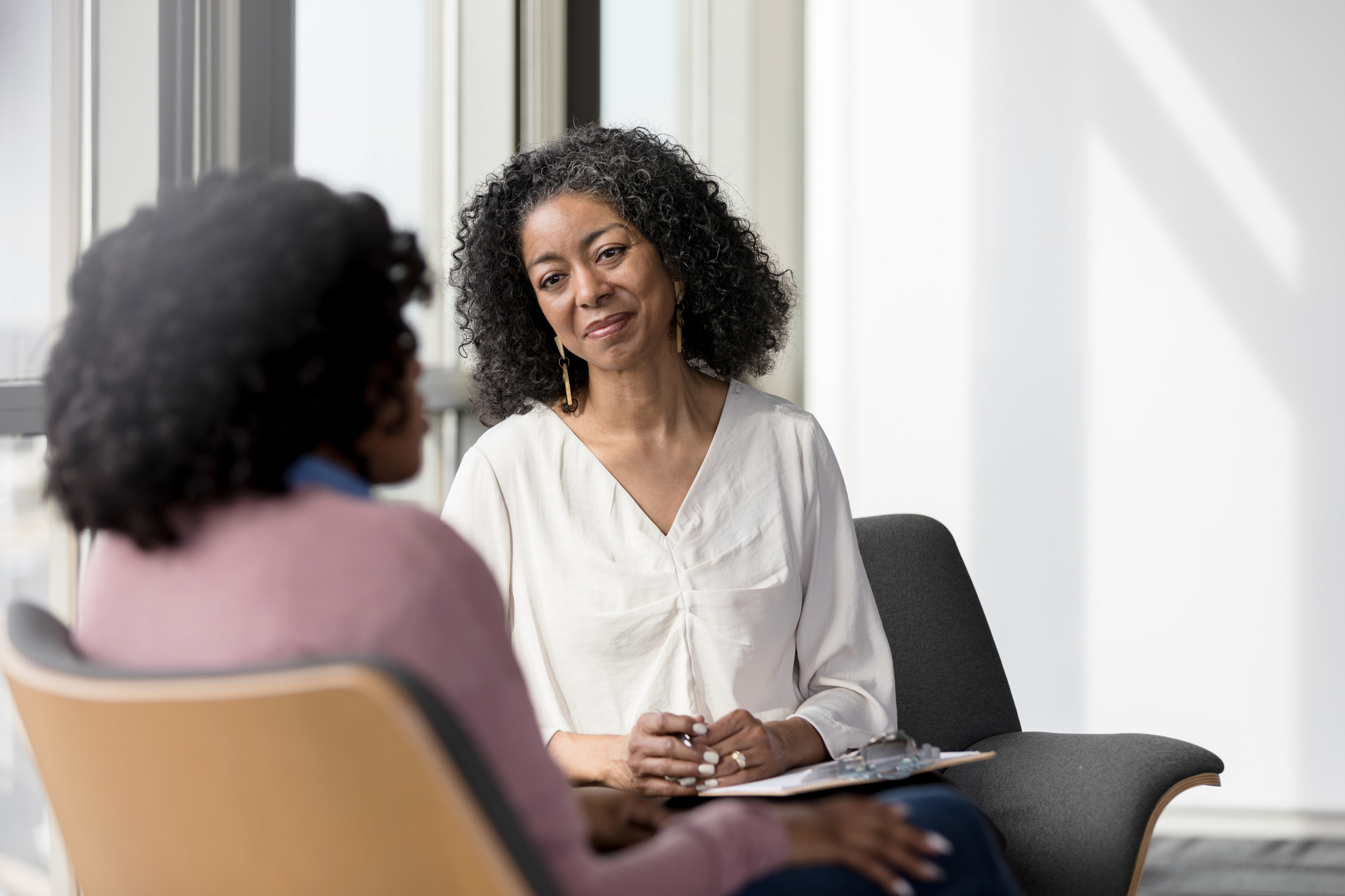 A Black therapist smiling calmly at a patient, who has her back turned to the camera