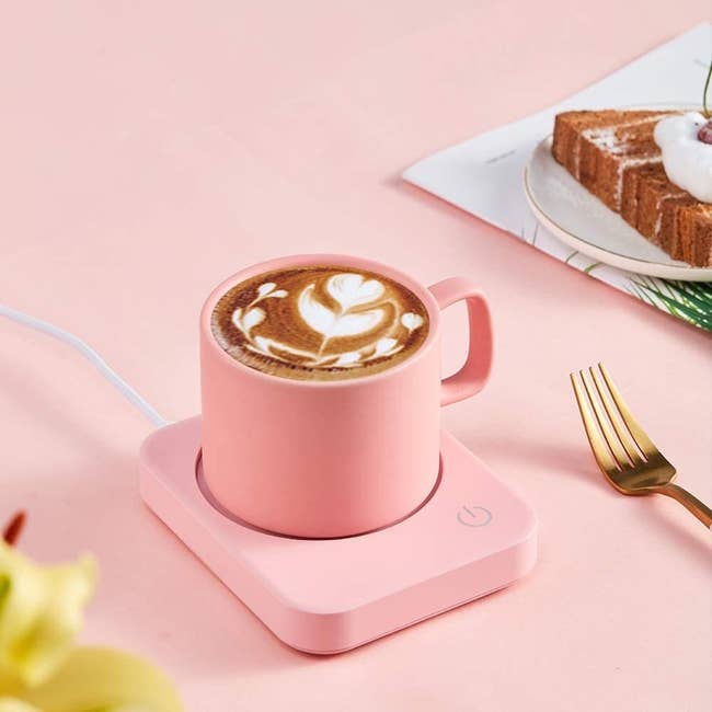 The pink version of the mug warmer with a pink cup of coffee on it on a desk