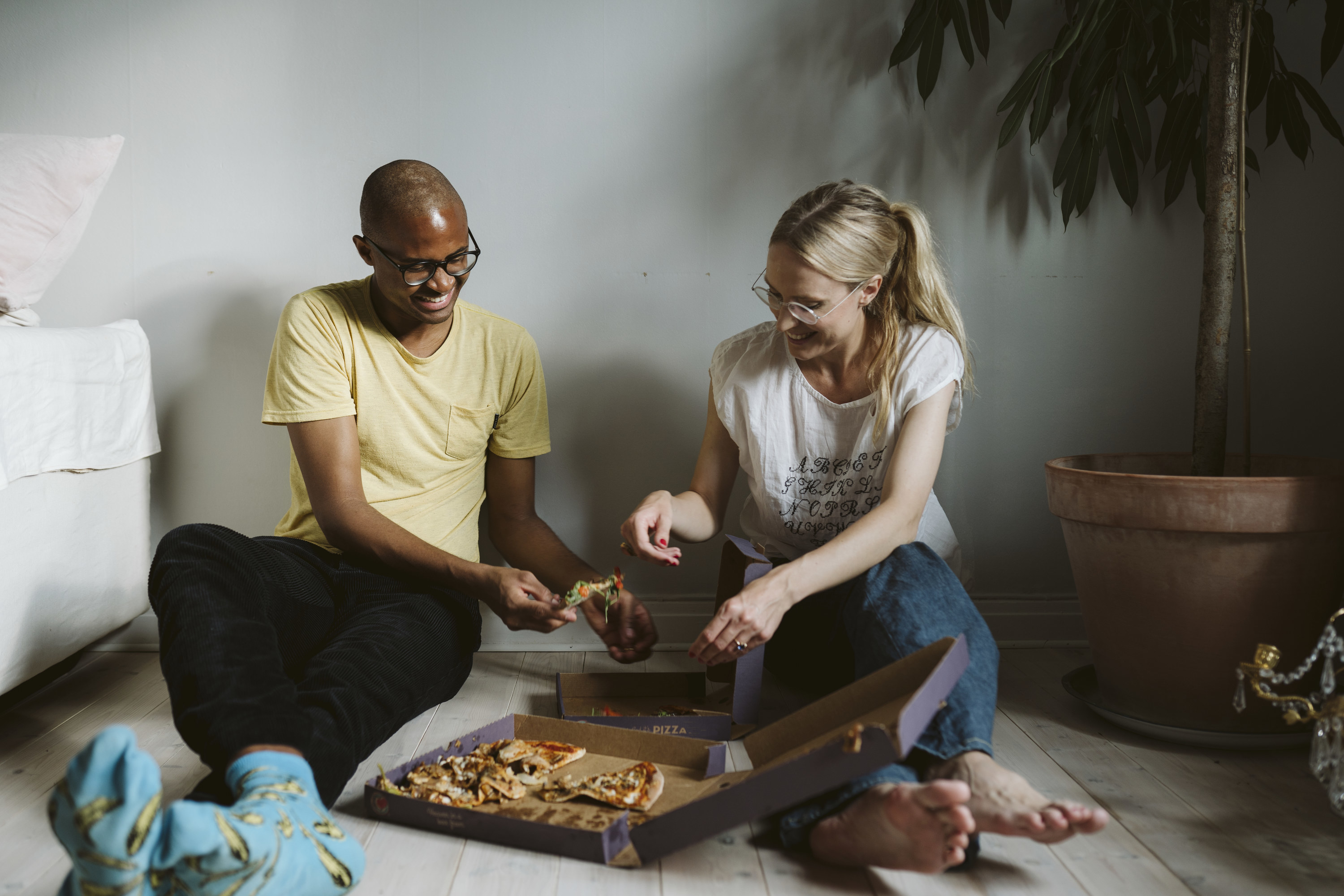 Two partners sitting on floor while eating delivery pizza out of a box