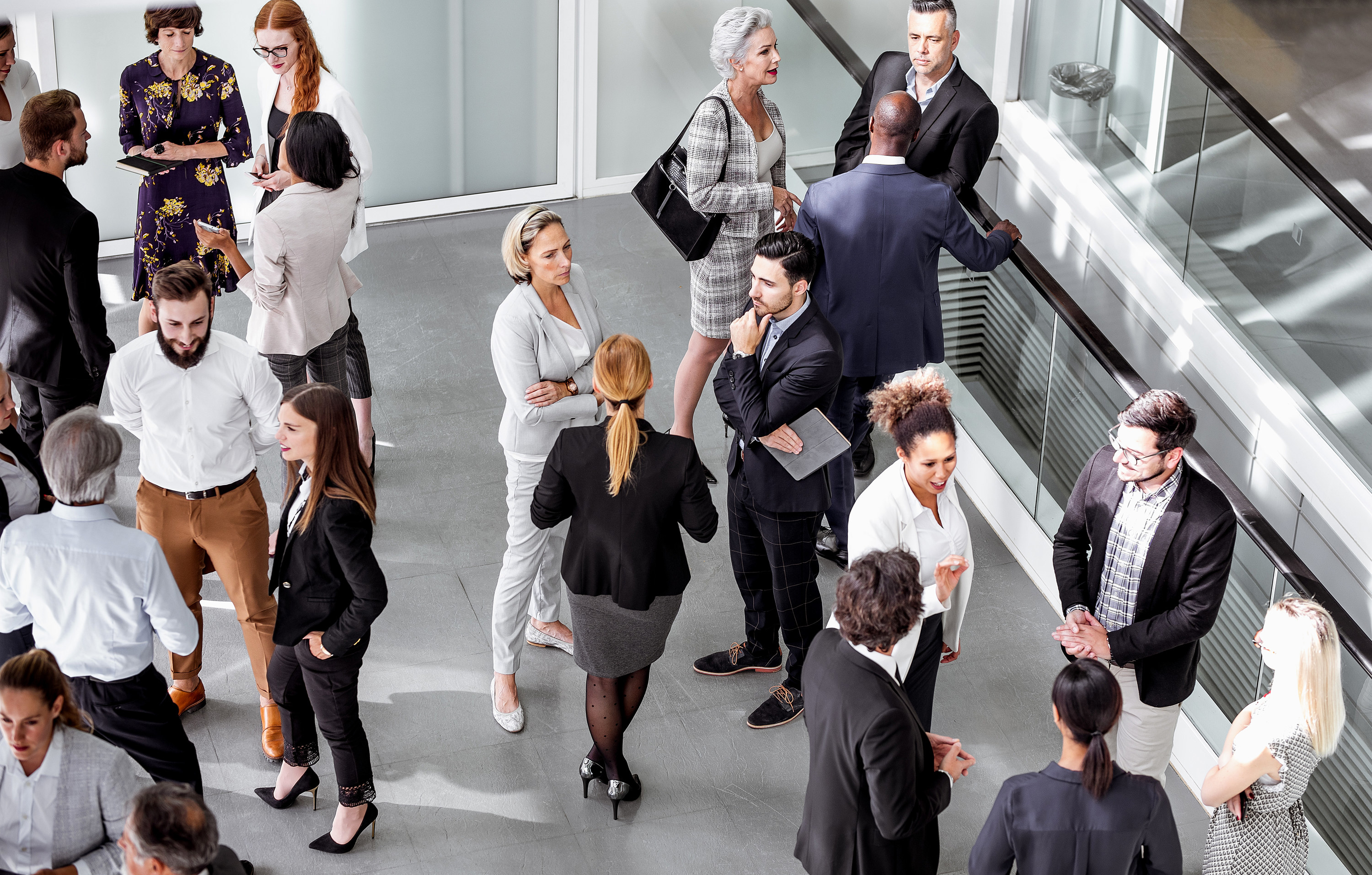 Room full of professionals wearing business outfits in a large conference room, talking in small groups