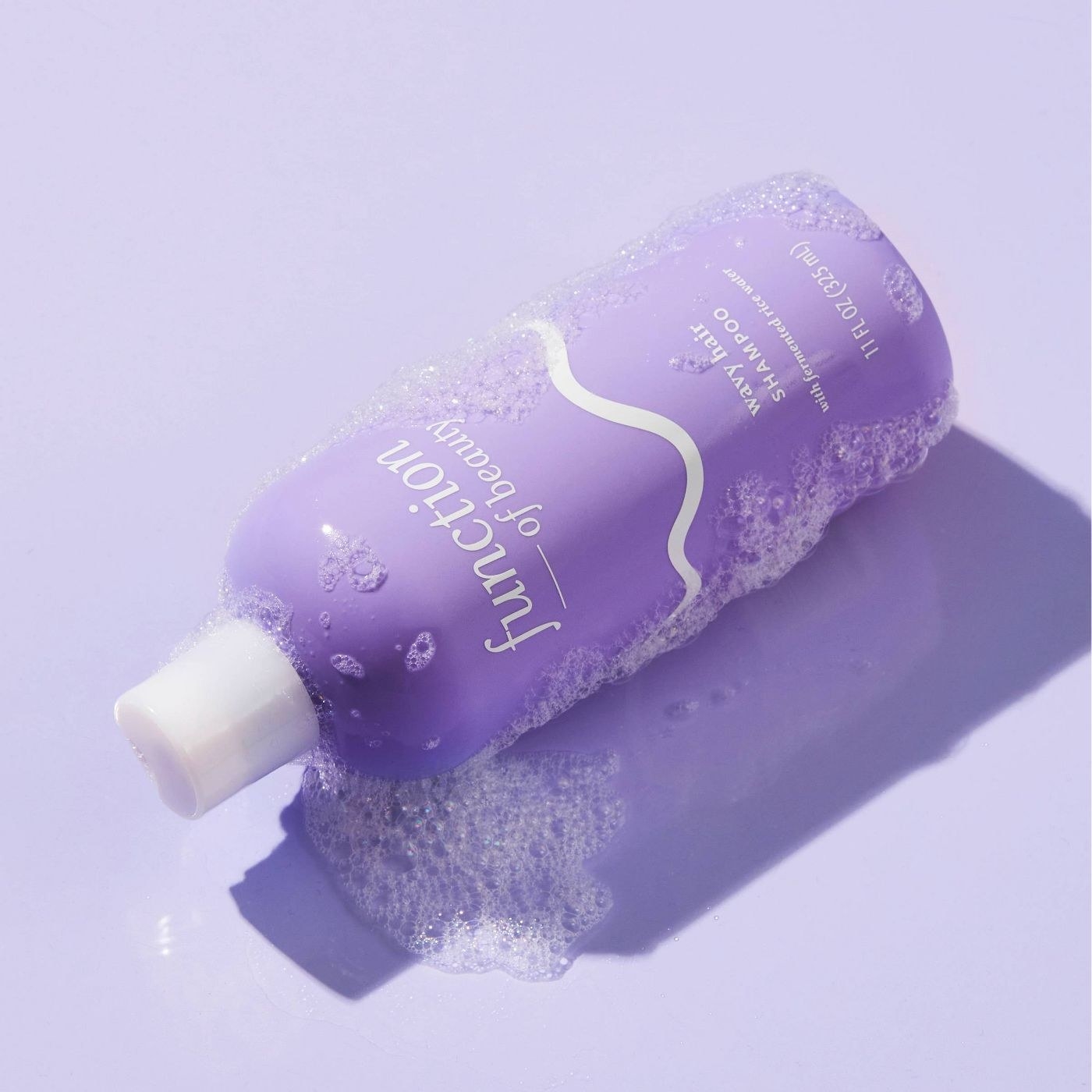A purple bottle of hair conditioner on a purple backdrop with soap suds