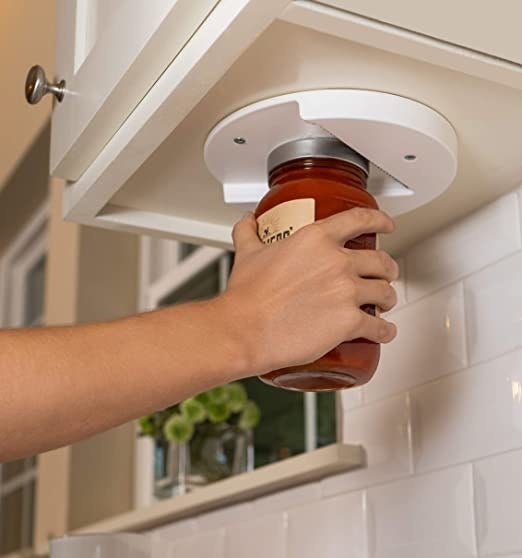 A person using the mounted jar opener to open a lid 