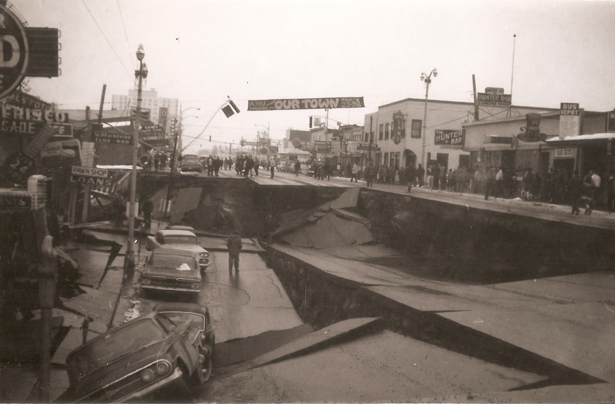 A destroyed street with a banner hanging over that says Our Town