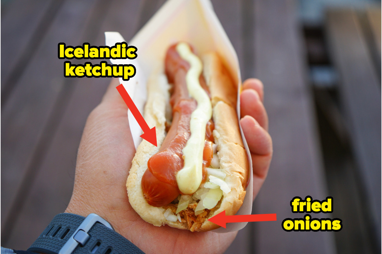 A hand holds a hot dog covered in mayo, ketchup, and fried onions