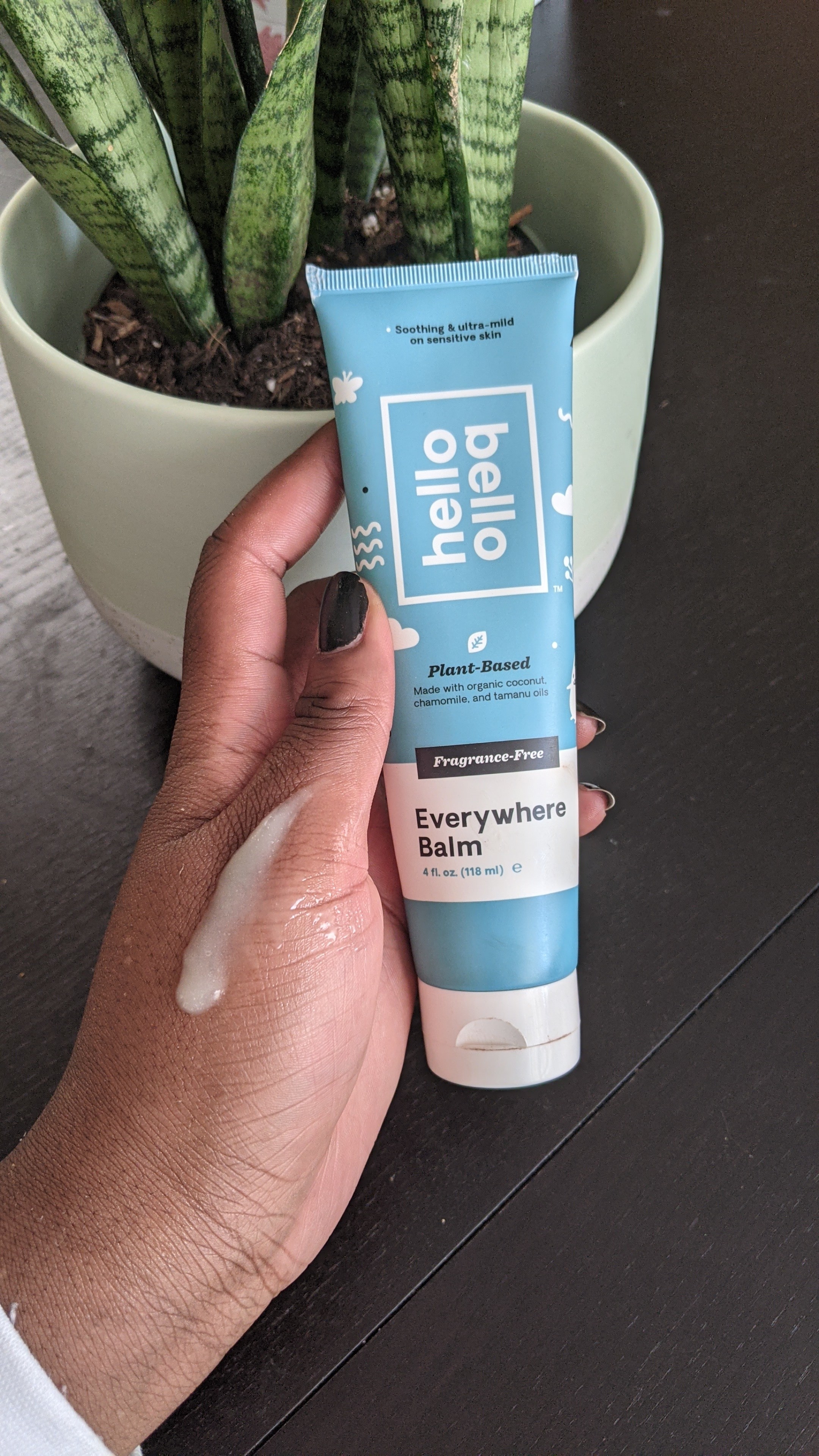 A person holding a tube of thick lotion with a swatch of product on their hand