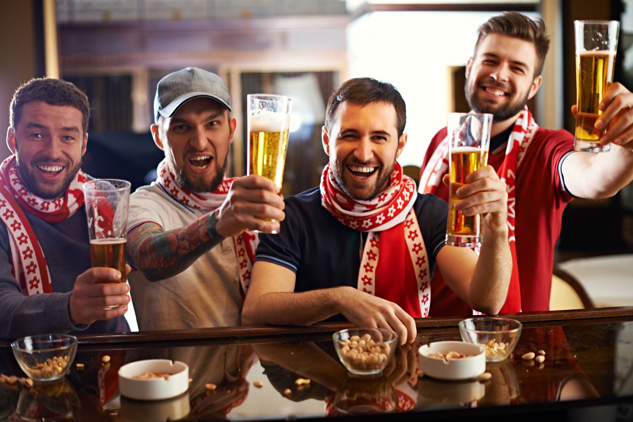 A group of men sitting down at a bar holding up their beers 