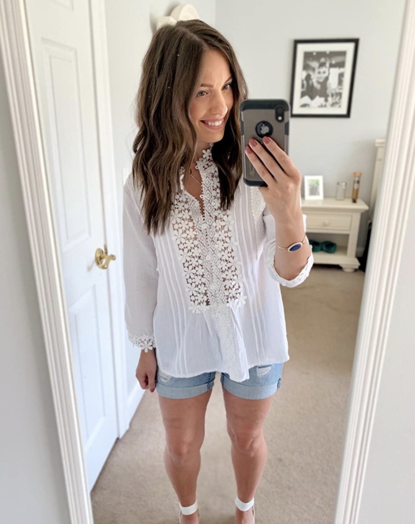 Person is wearing a white blouse with floral detail and denim shorts