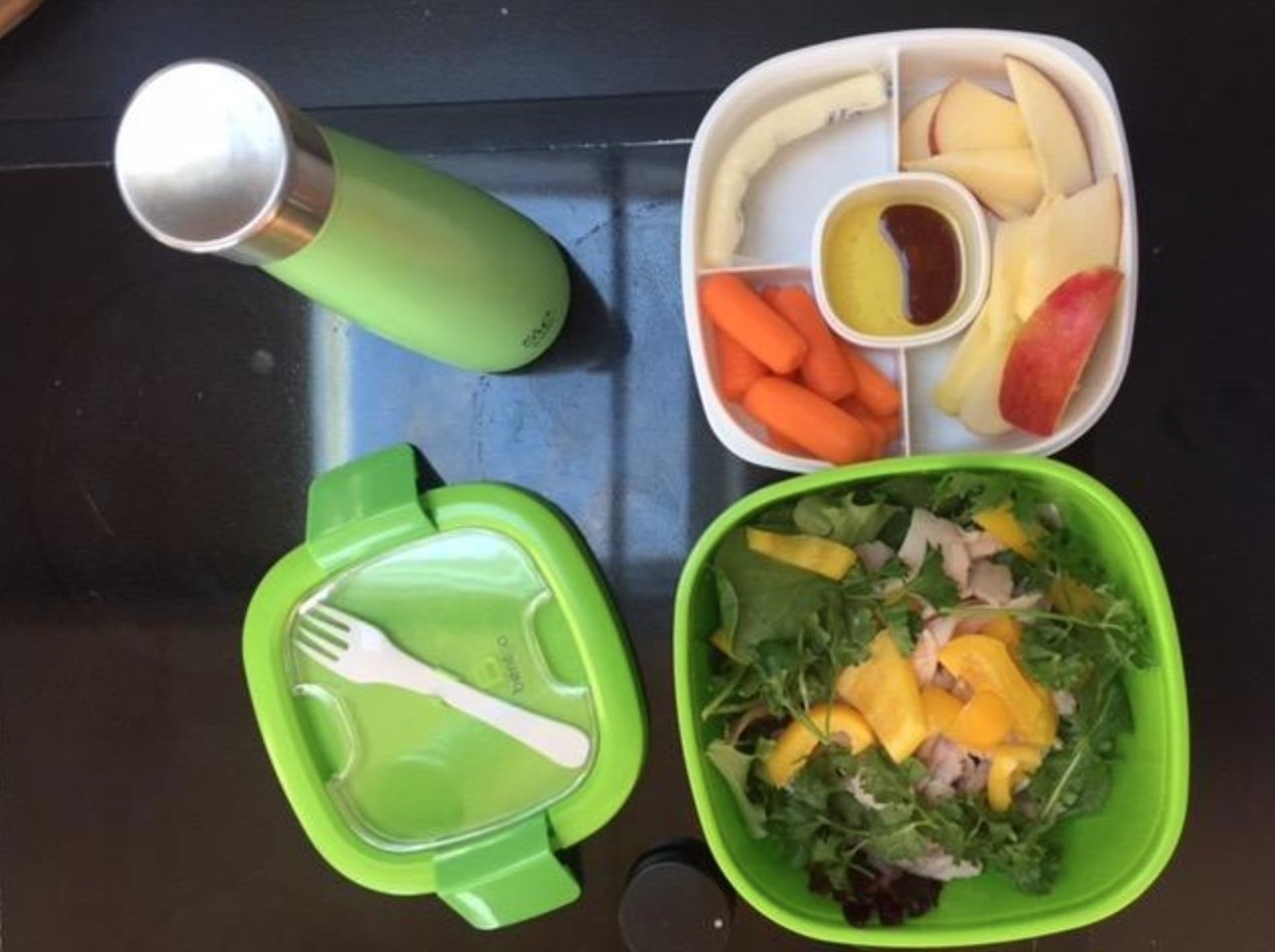  bento box style lunch container in green, holding salad in the bottom and veggies and dressing on the top divided portion