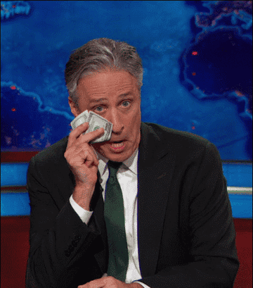 Jon Stewart dabbing at his eyes with a 100 dollar bill