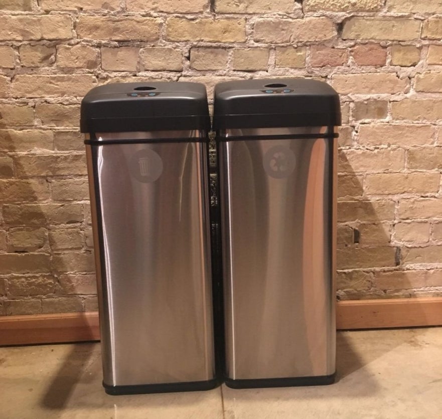 The reviewer&#x27;s photo of two side by side touchless stainless steel trash cans with black lids
