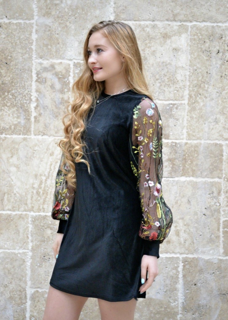 Person is wearing a black dress with mesh sleeves that have floral details on them