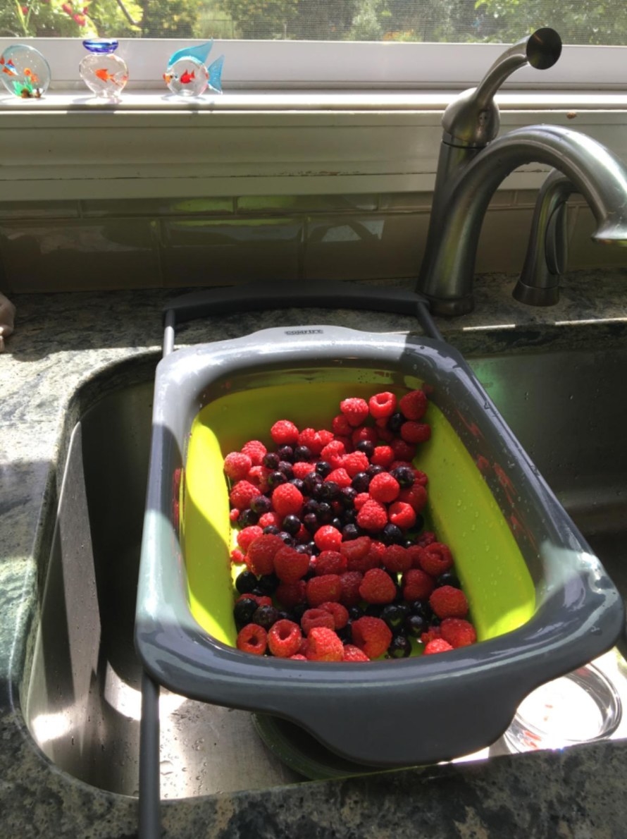 The reviewer&#x27;s photo of the green collapsable strainer in their sink