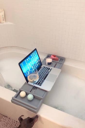 reviewer pic of the bathtub caddy over a bubble bath with a wine glass and laptop on it 