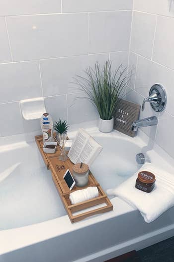 reviewer pic of a bathtub caddy over a bubble bath with a book, phone, and other items on it