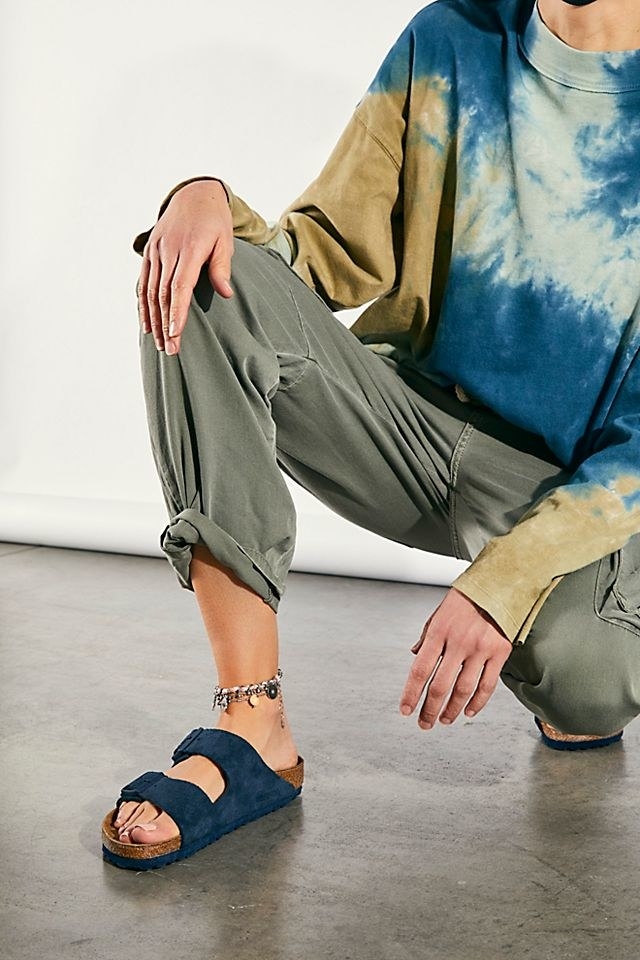 model wears navy Birkenstock sandals with green cargo pants and tie-dye tee