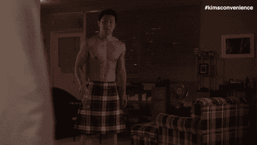 A fit Asian man shirtless in a kilt looks awkward and says &quot;hey&quot;