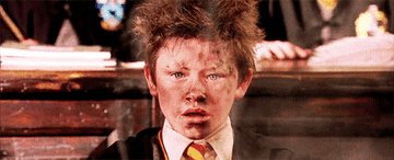Seamus Finnigan with a shocked face on his soot-covered face. His hair looks electrocuted and smoke rises in front of his face, which is missing eyebrows