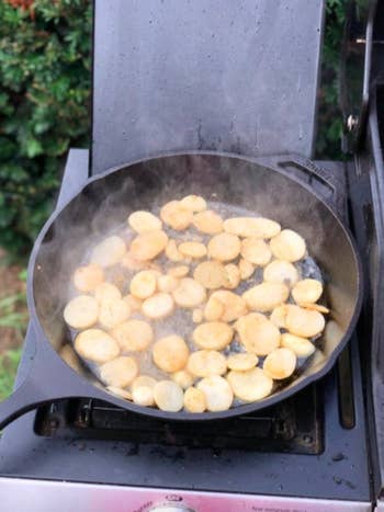 a cast iron skillet cooking potatoes on a grill