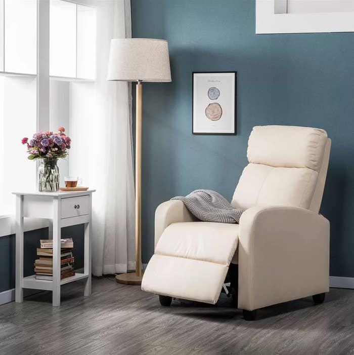 The home theatre individual seat in beige next to a tall floor lamp