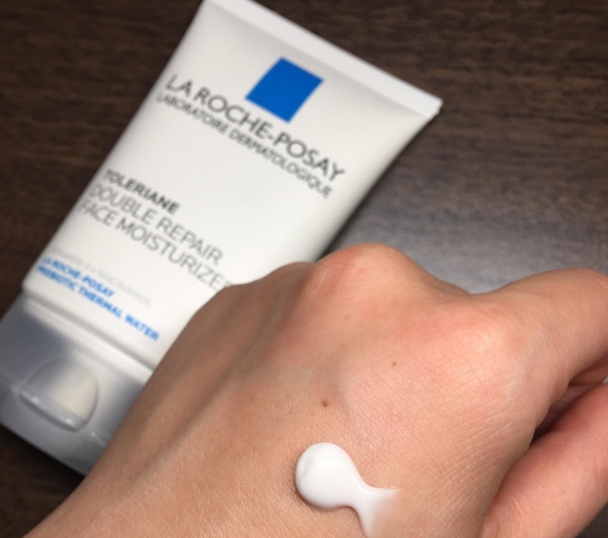 a reviewer photo of a hand with a dollop of white cream on the back next to the moisturizer bottle 