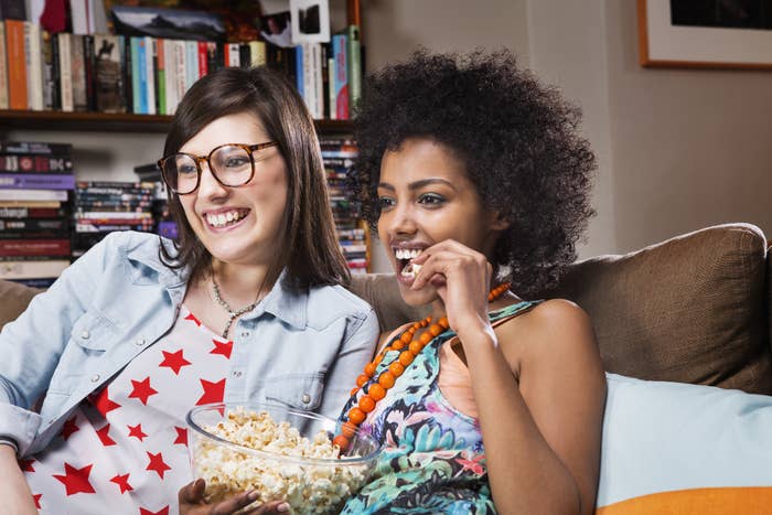 Two women eating popcorn and watching TV