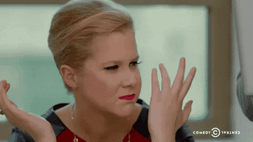 Amy Schumer chews slowly with her hands thrown up and eyes squinted in annoyed confusion