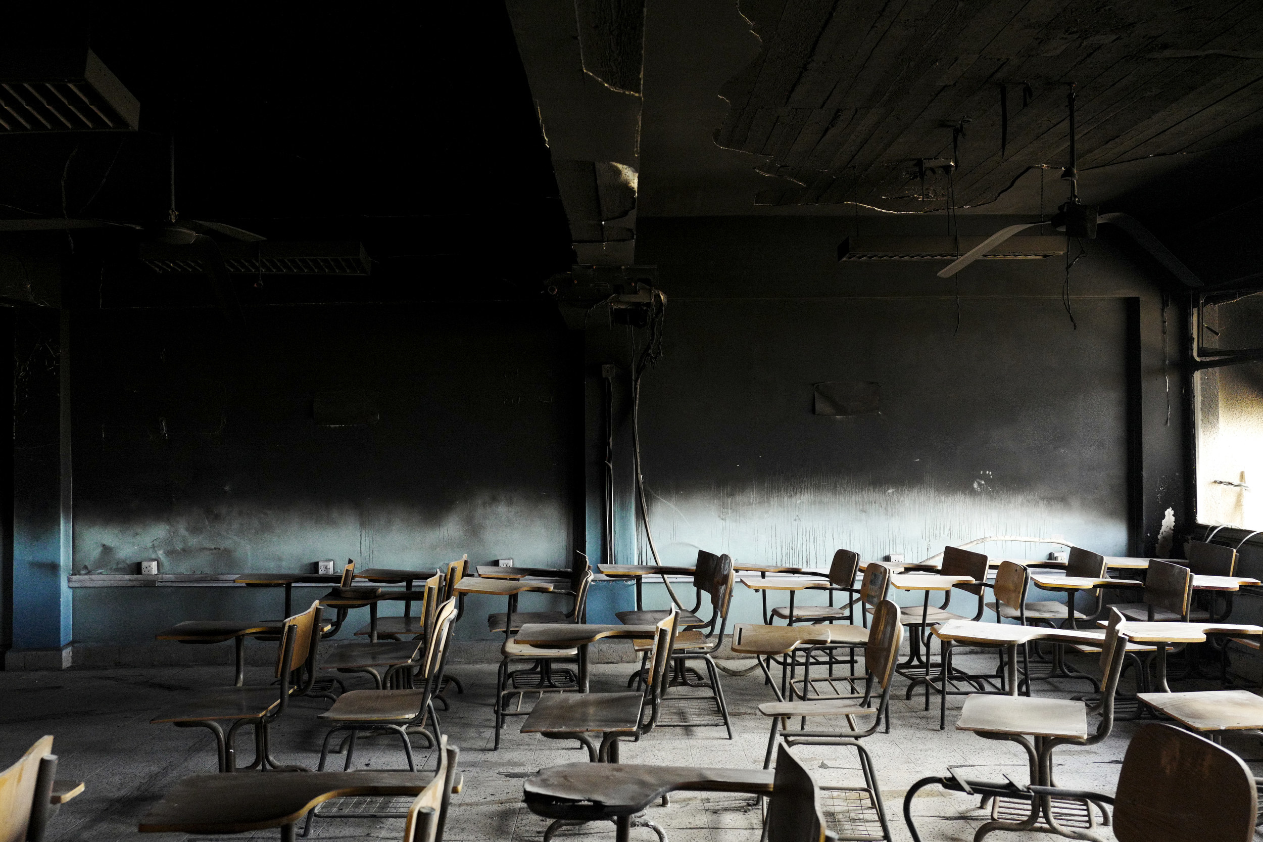 An empty school room with desks out of order and charred walls