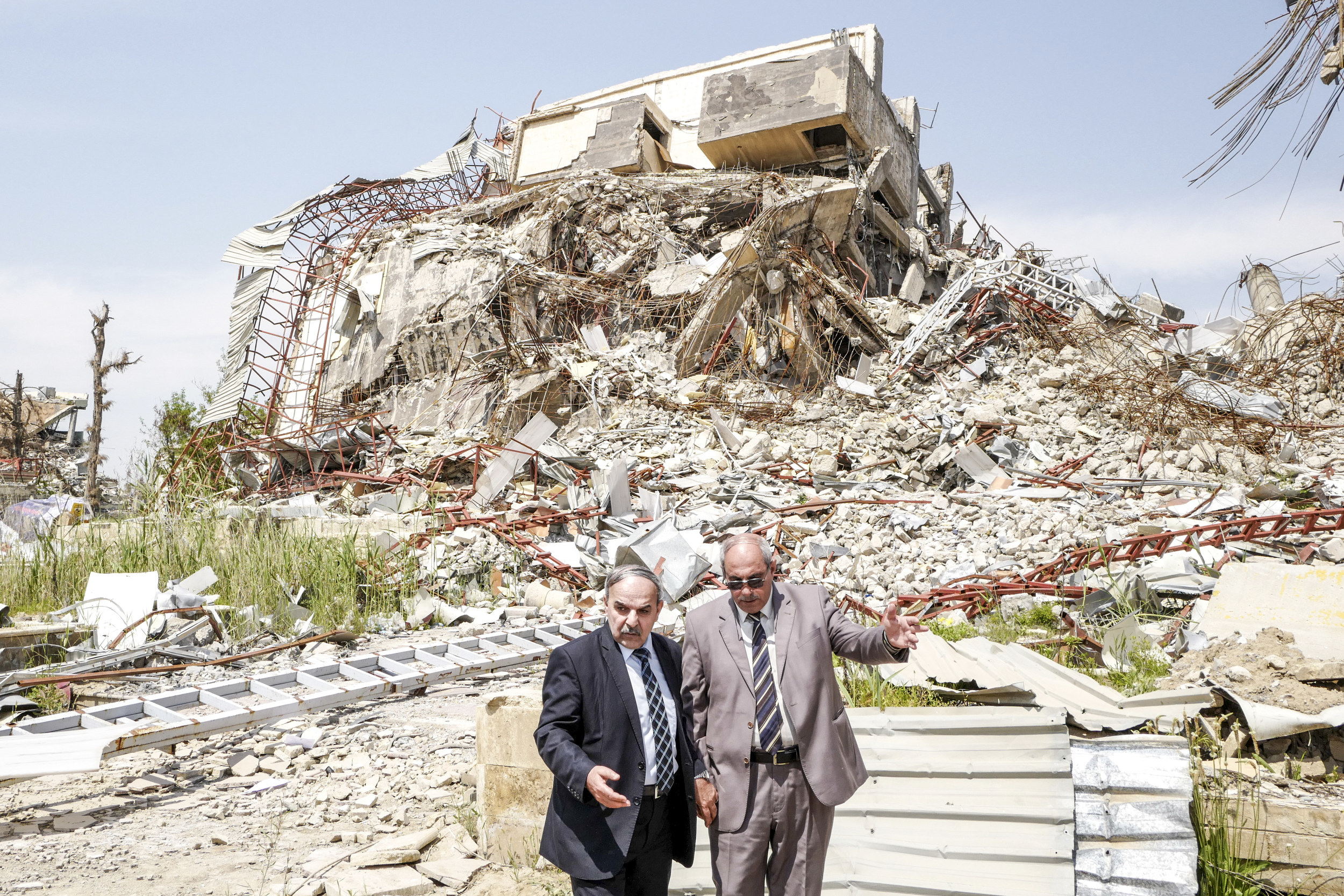 Two men in suits in front of a massive pile of rubble