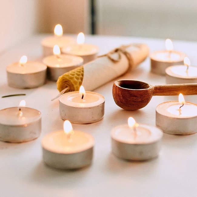 Several tiny candles aflame beside a wooden spoon and beeswax 