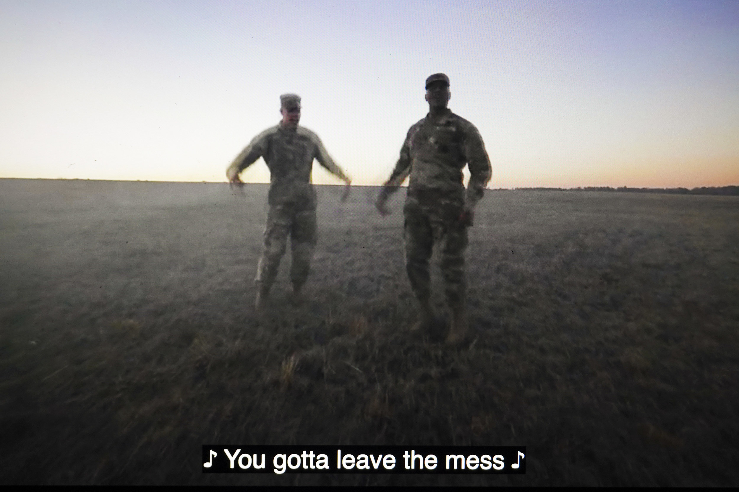 Two men in fatigues dancing in a  video with closed captioning that reads &quot;You gotta leave the mess&quot;